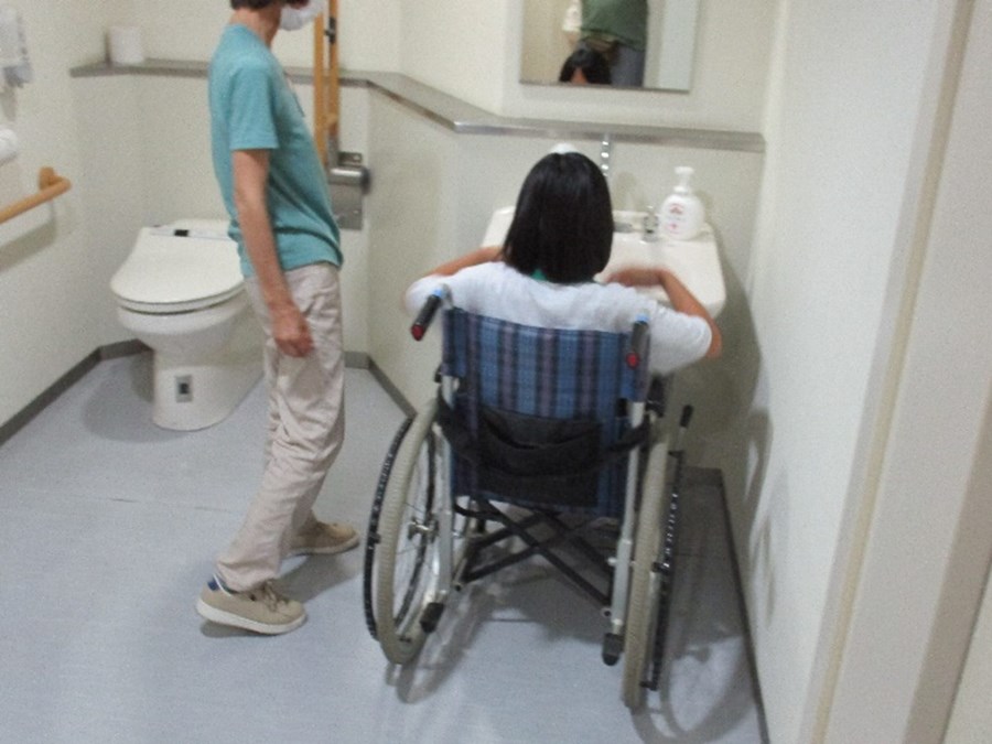 車いすに乗った子どもがトイレの洗面台の前で手を洗う体験をしている画像です。